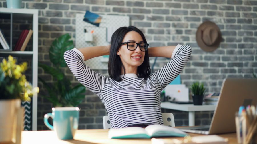 A woman leaning back from her desk with her hands behind her head, relaxed and smiling after simplifying her finances