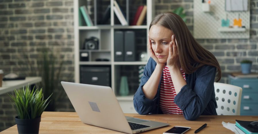A woman at her desk resting her head in her hands while looking at her laptop, representing the stress of carrying high-interest credit card debt