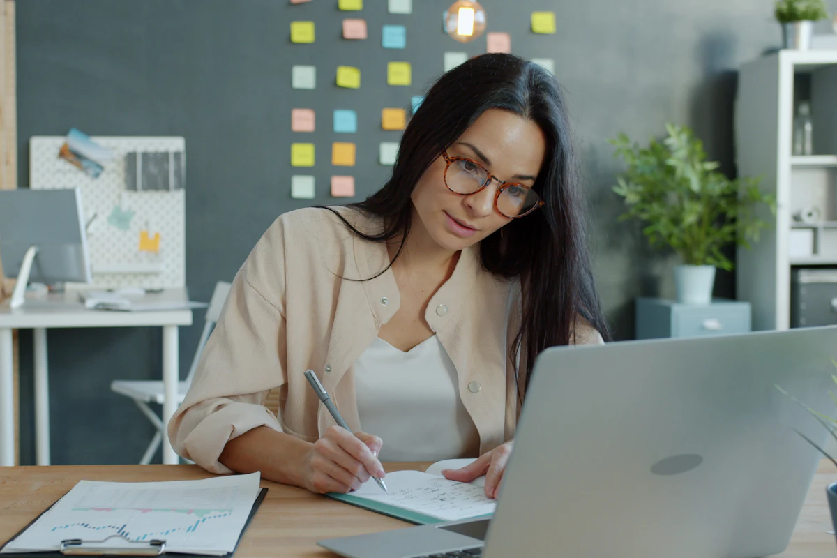 Woman at a home desk calmly writing a short repayment plan next to her laptop after covering an unexpected bill