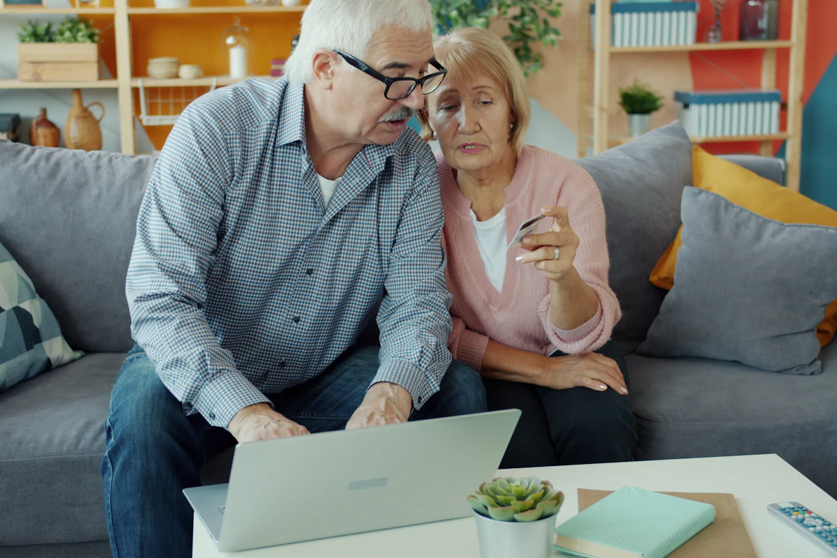 Older couple on a sofa looking at a laptop together, the woman holding a bank card