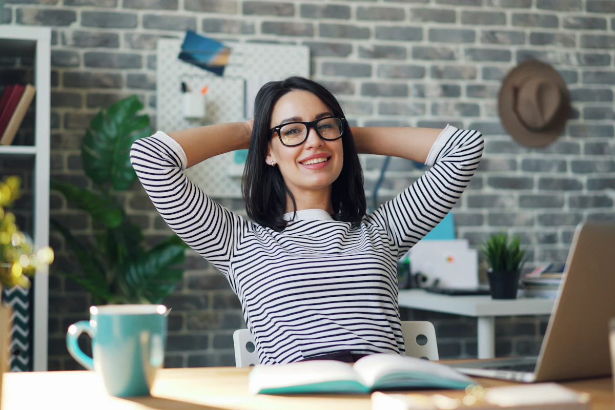 Woman leaning back and smiling at her desk with a coffee mug and an open notebook