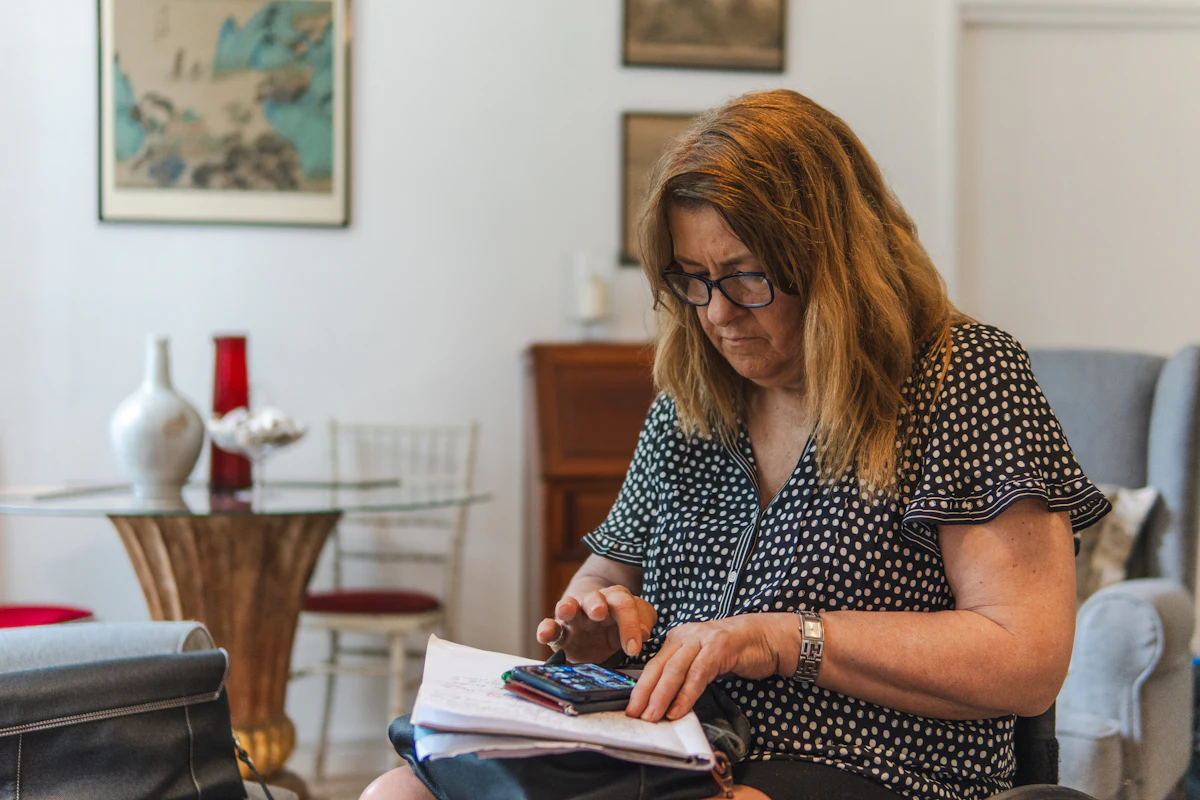 Woman at home working through her monthly budget with a calculator and a notebook